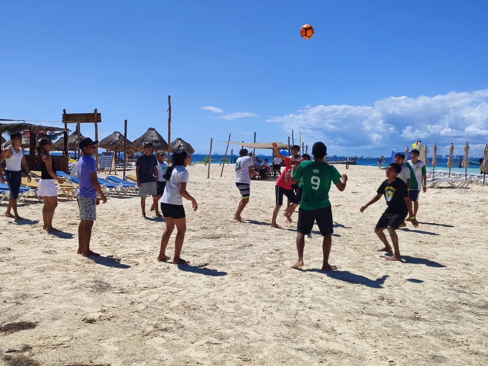 Un grupo de jóvenes juega con un balón en la playa durante una salida del taller.