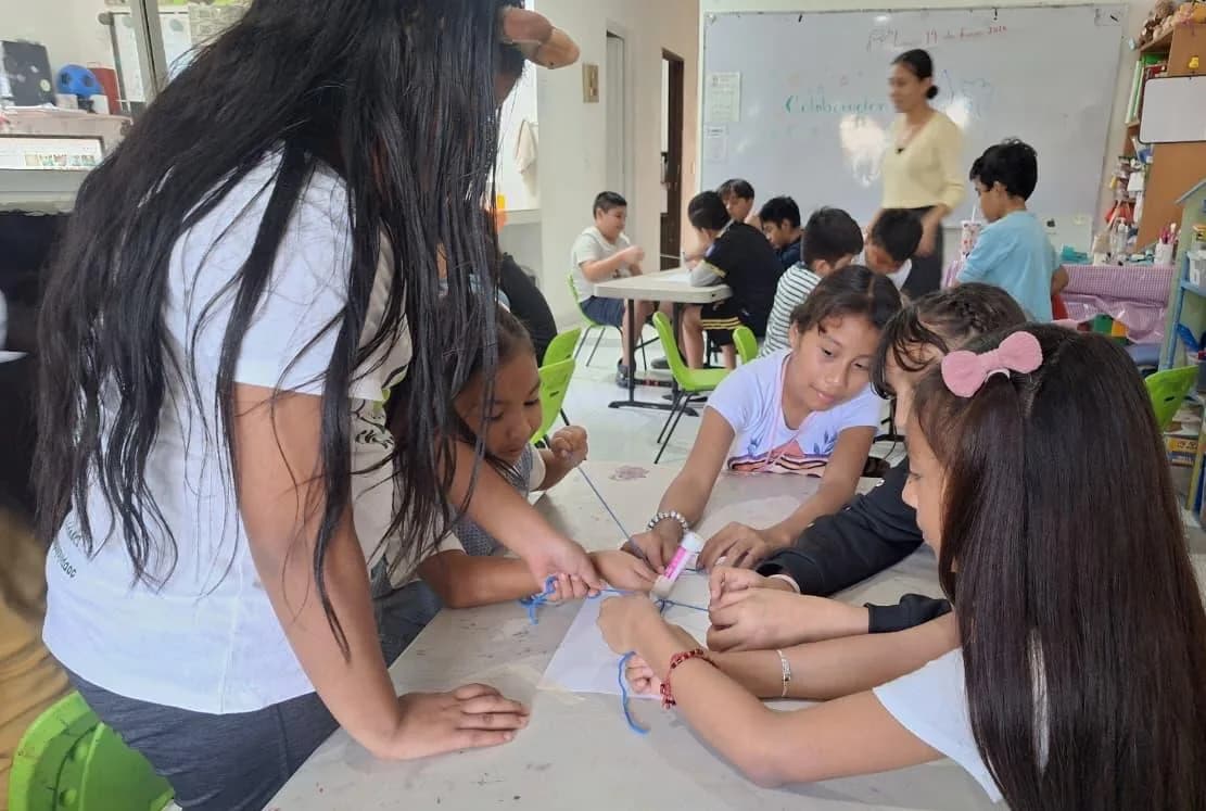 Una tallerista acompaña a niñas y niños que recortan y arman material didáctico en el salón.
