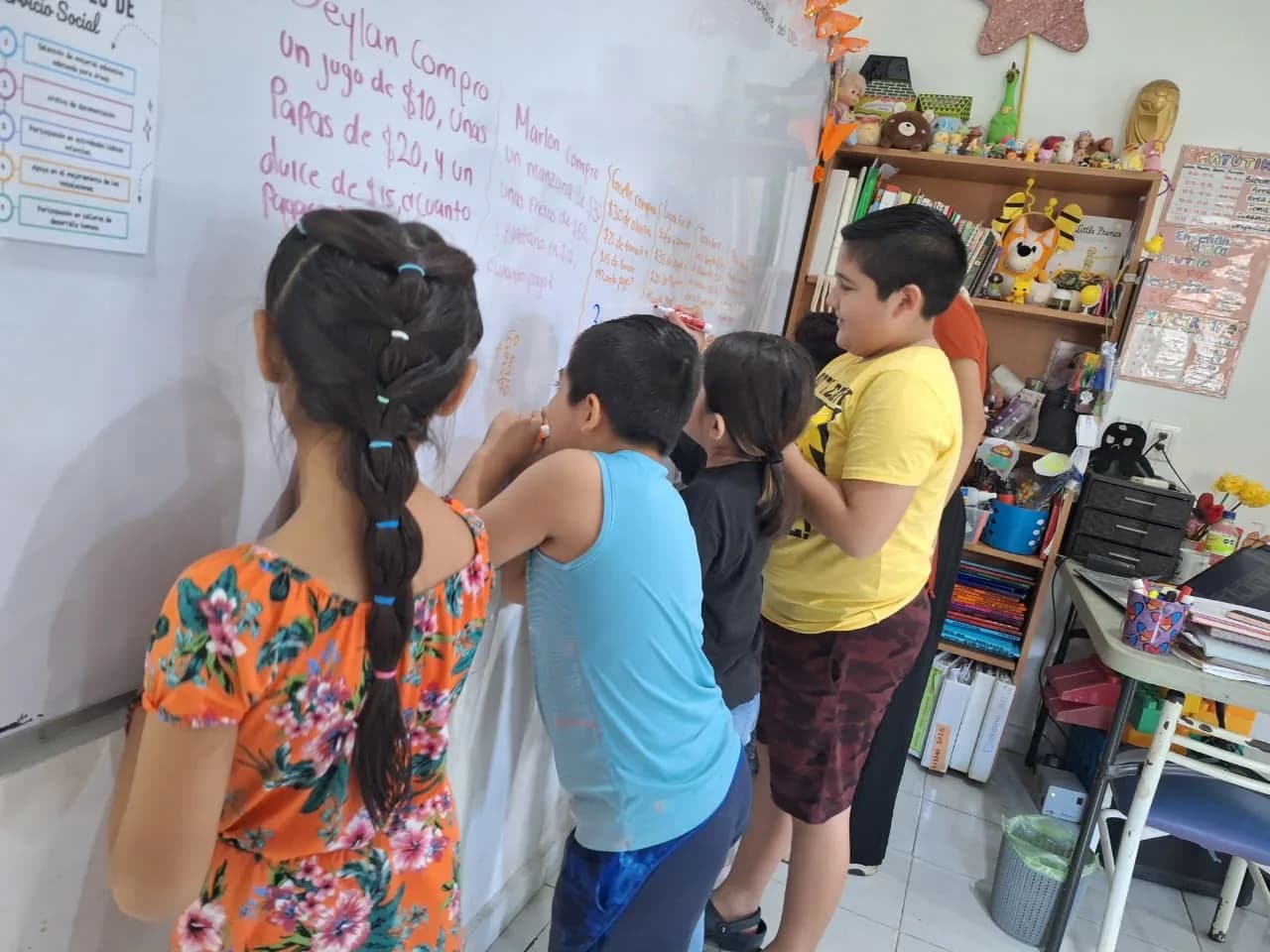 Cuatro niñas y niños resuelven frente al pizarrón un problema escrito a mano.