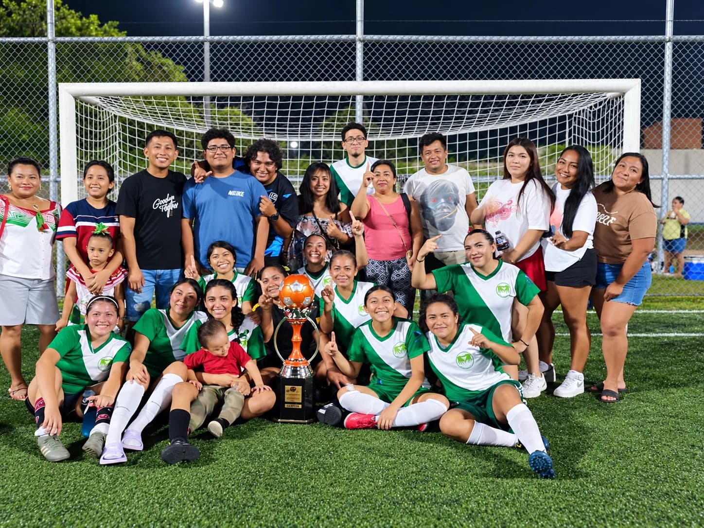 Jugadoras, familias y entrenadores posan con el trofeo frente a la portería.