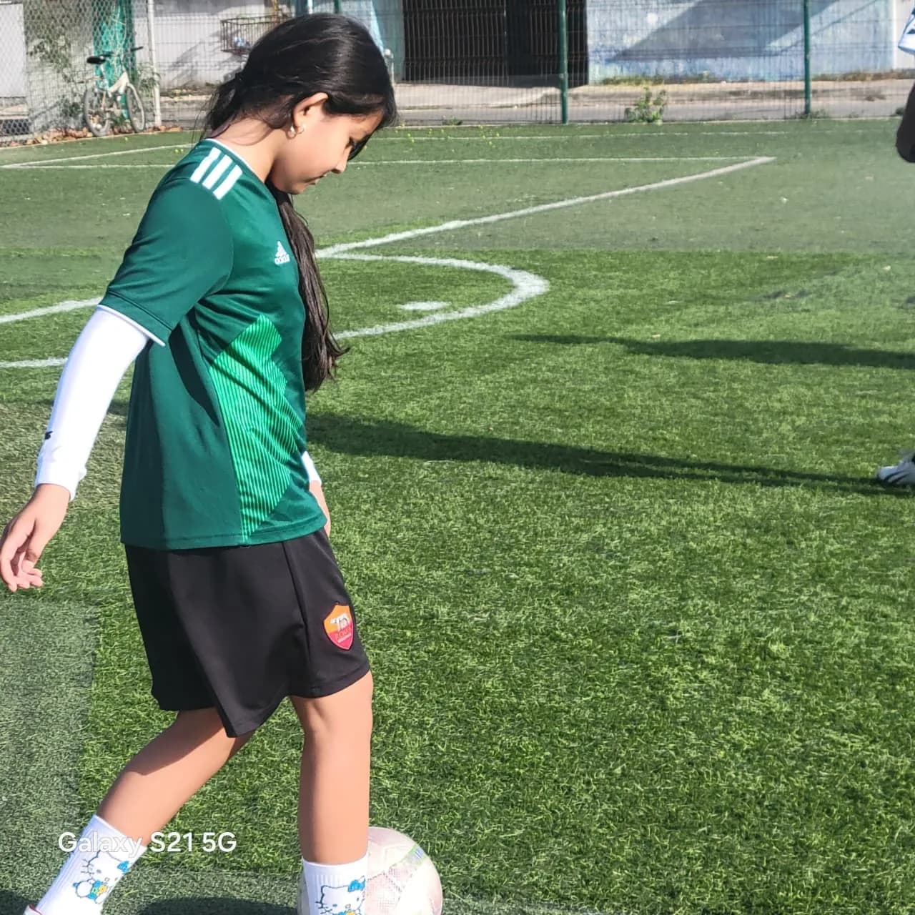 Una niña con uniforme verde conduce el balón en la cancha.