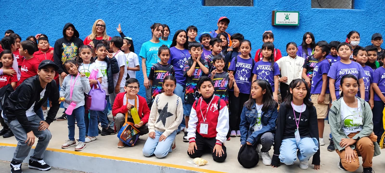 Niñas, niños y jóvenes posan en grupo frente a un muro azul durante una salida.