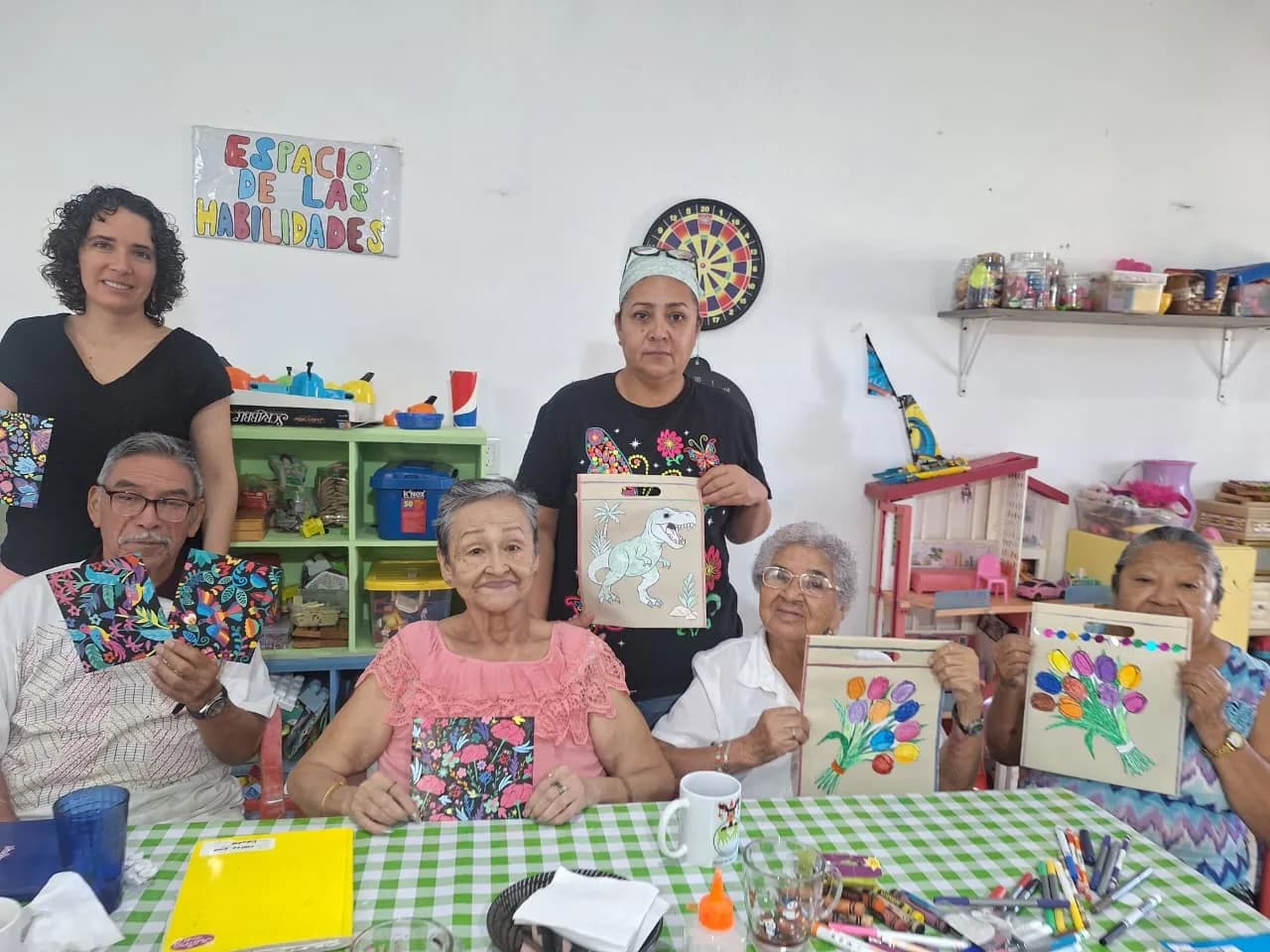 Personas adultas mayores muestran los cuadros que pintaron, acompañadas por las talleristas.