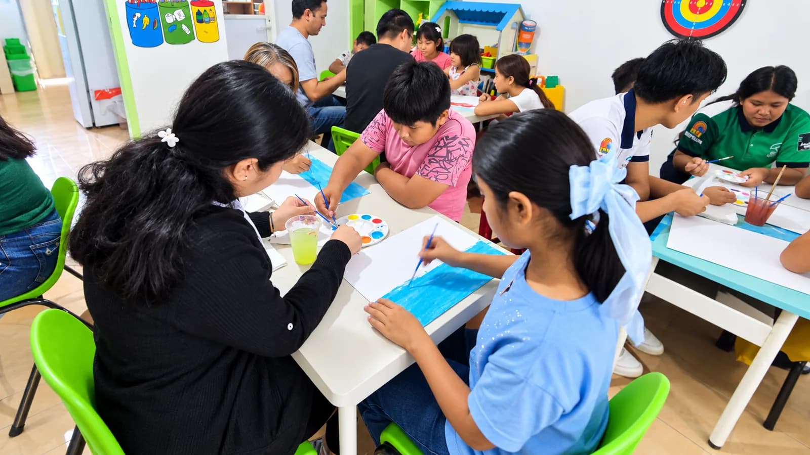 Niñas, niños y talleristas pintan con acuarela en varias mesas de la ludoteca.