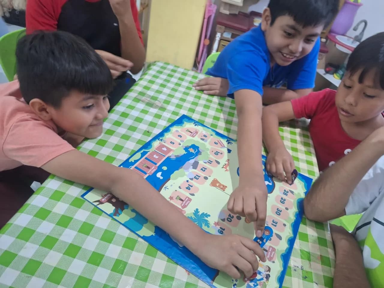 Tres niños juegan un juego de mesa sobre un mantel de cuadros verdes.