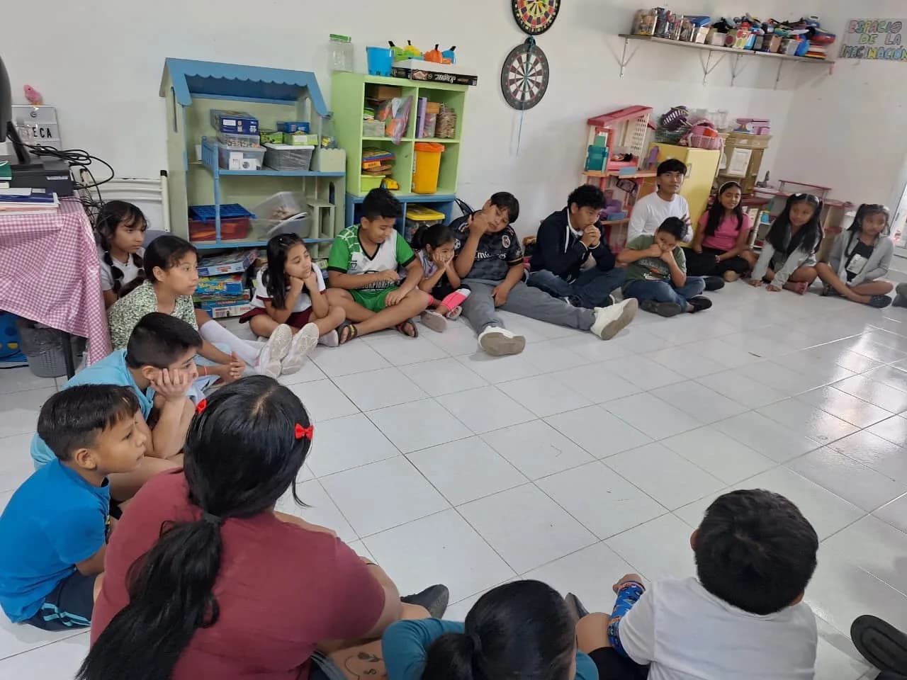 Niñas y niños sentados en círculo en el piso de la ludoteca durante una actividad grupal.