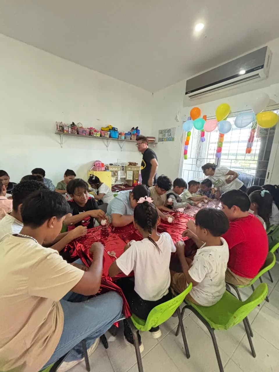 Un grupo de niñas y niños trabaja con material de manualidades en una mesa decorada con globos.