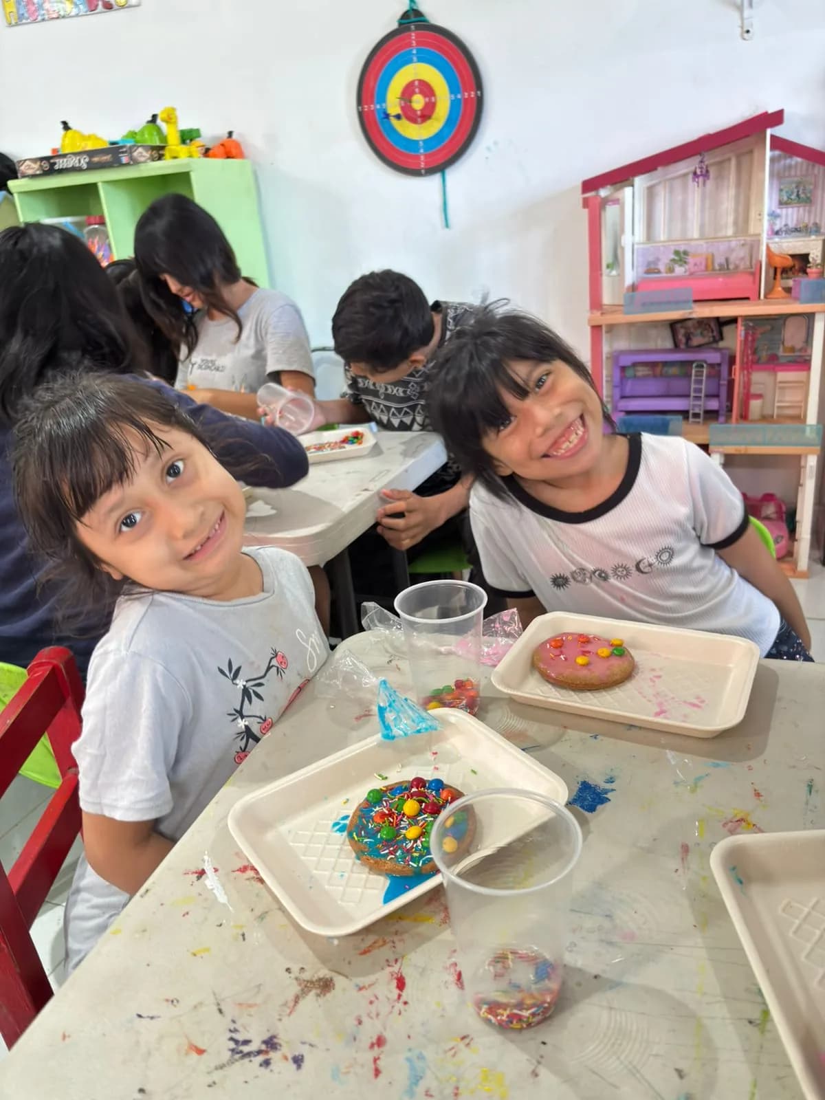 Dos niñas sonríen junto a las galletas que acaban de decorar con betún y dulces de colores.