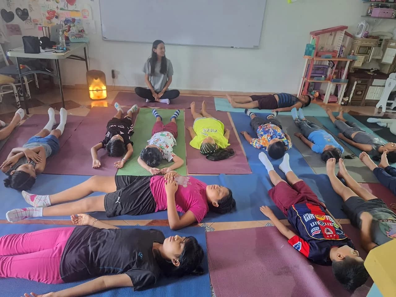Niñas y niños acostados sobre tapetes durante un ejercicio de relajación guiado por una tallerista.