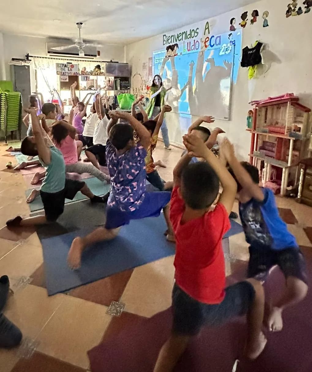 Niñas y niños estiran los brazos en una activación física frente al mural de bienvenida a la ludoteca.
