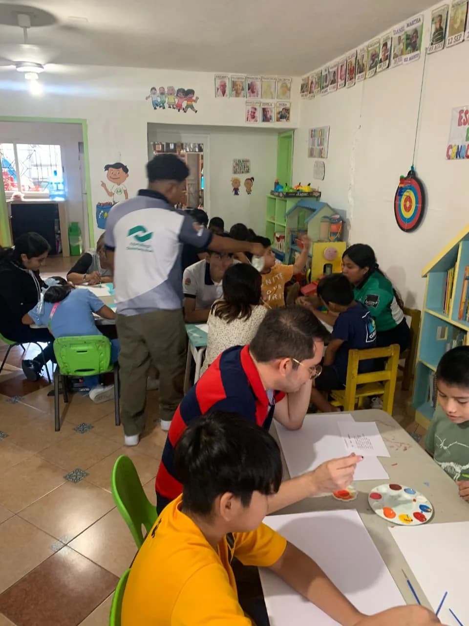 Estudiantes uniformados acompañan a niñas y niños en una sesión de pintura en el salón.