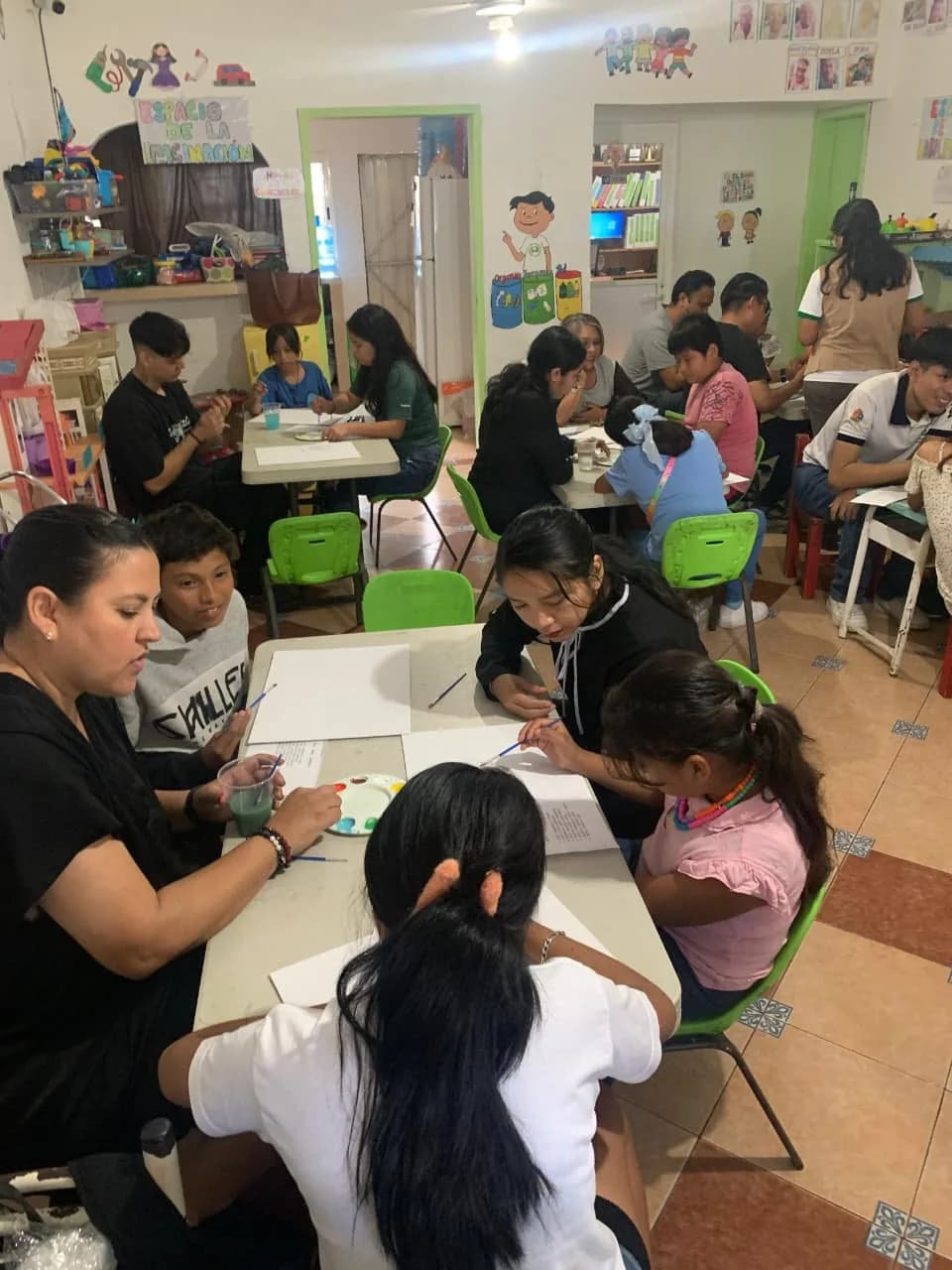 Voluntarias y familias pintan juntas en varias mesas de trabajo del salón.