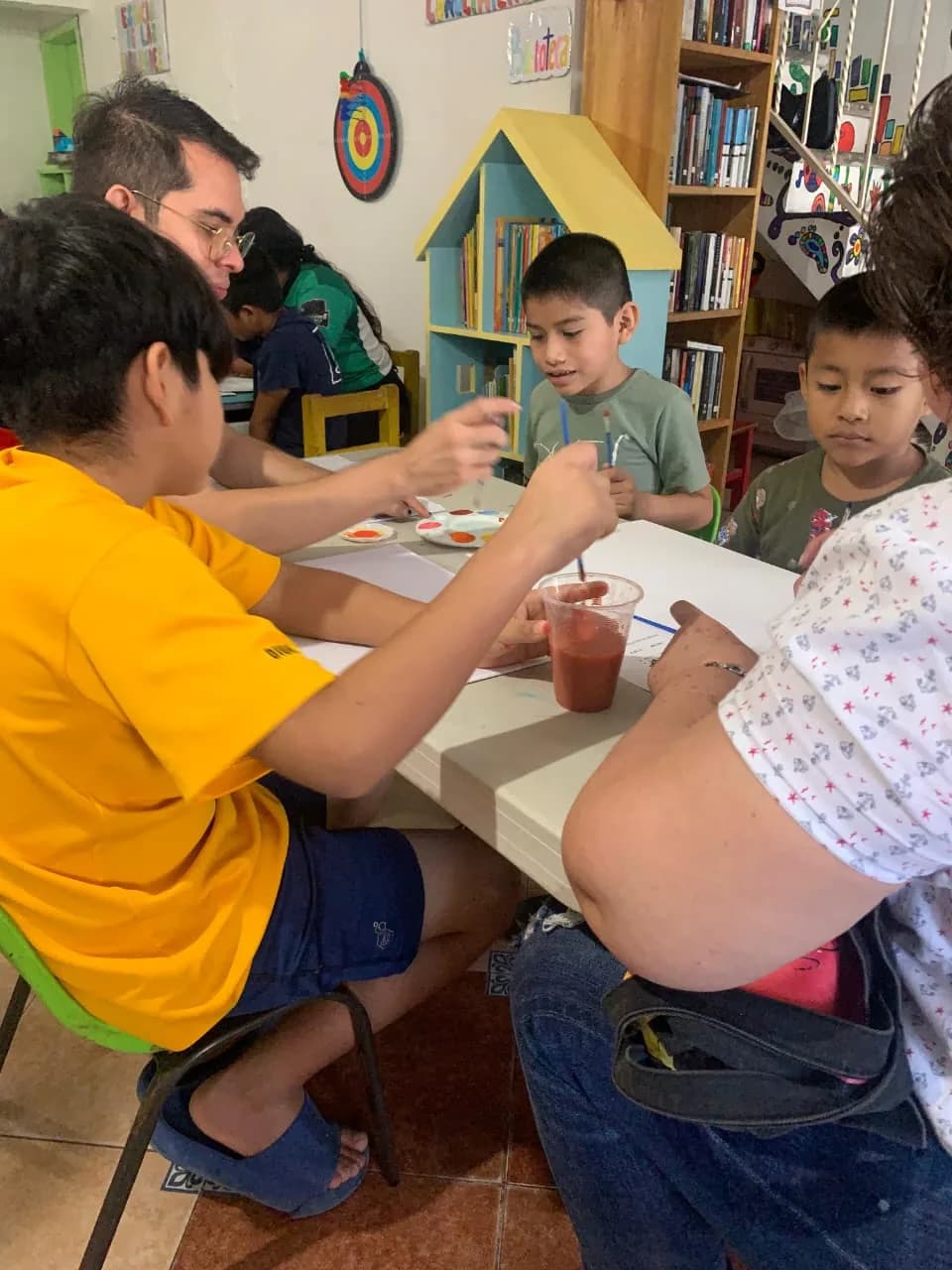 Un voluntario acompaña a dos niños mientras mezclan pintura en la mesa.