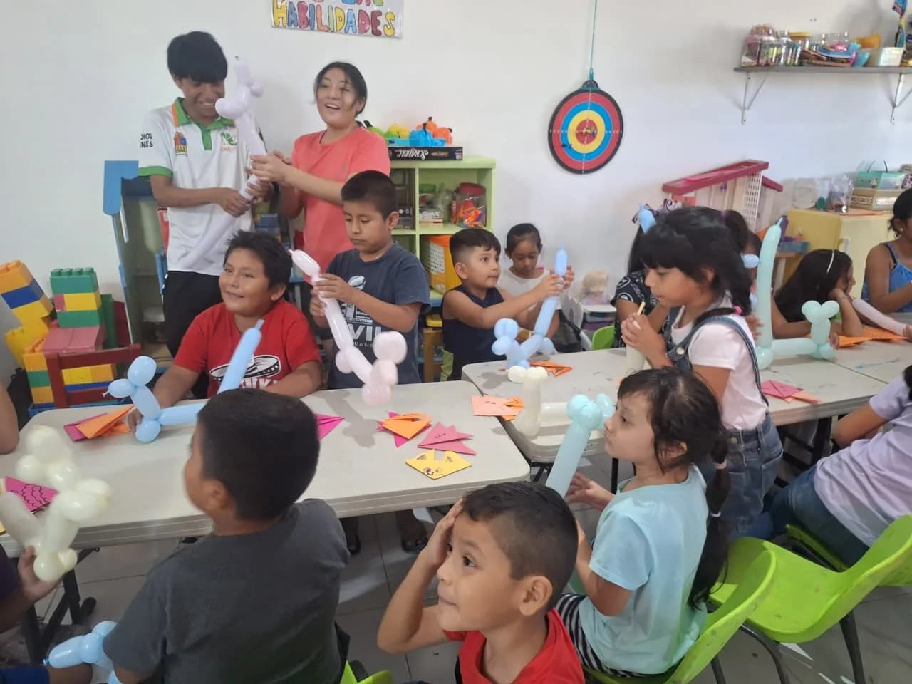 Dos voluntarios reparten figuras de globos entre niñas y niños en el salón.